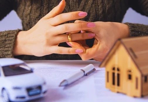 Handen met trouwring boven financiële papieren en een houten huisje